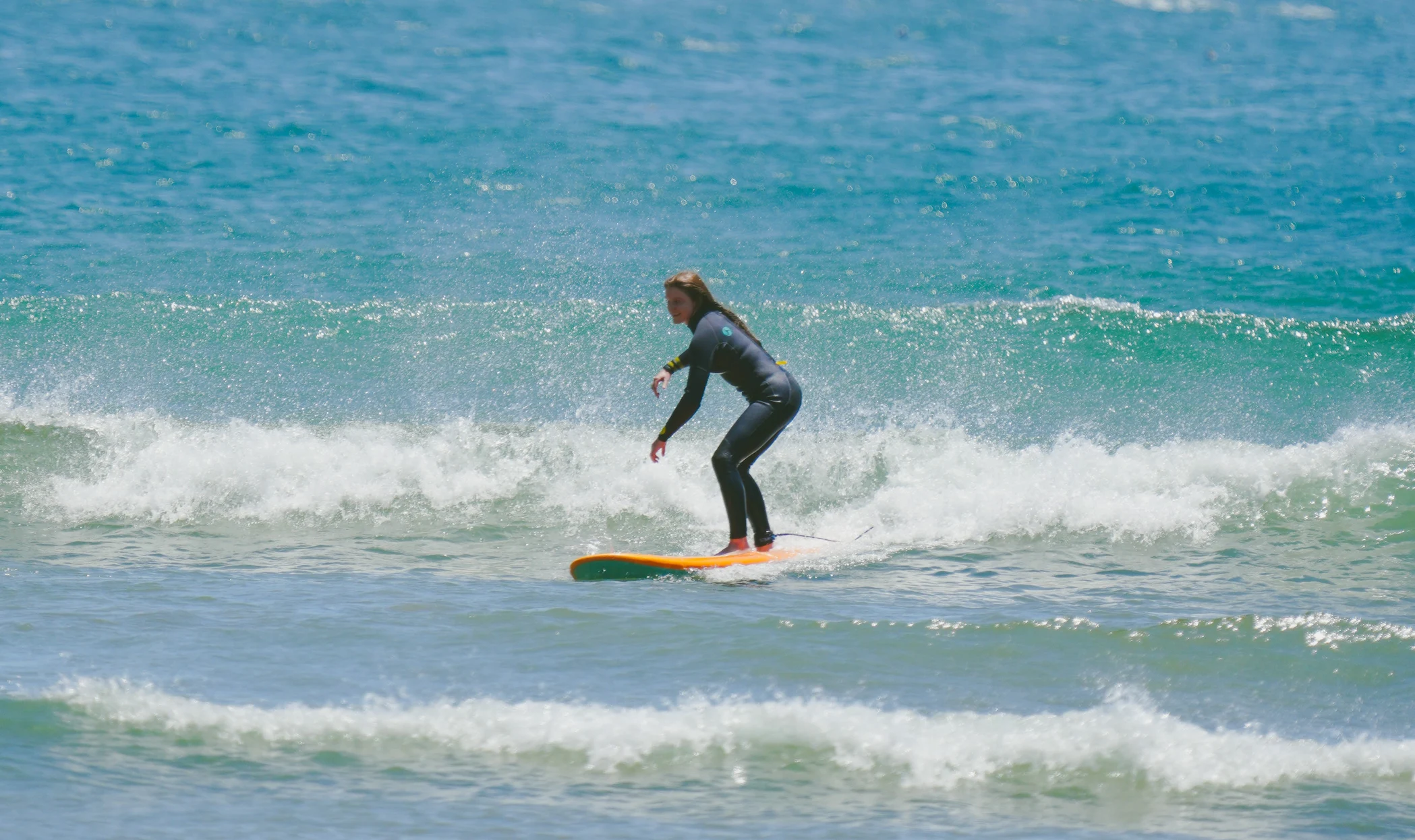 A surfer in a dark wetsuit rides a breaking wave on a yellow surfboard in clear blue water